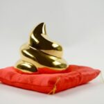 sur un coussin de satin rouge, une sculpture dorée représentant un étron