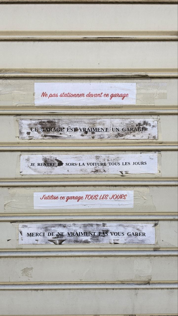 sur ce qu'on devine ĂȘtre une porte de garage baissĂ©e, sur chaque lamelle du portail dĂ©roulant, un message collĂ© : ne pas stationner devant ce garage CE GARAGE EST VRAIMENT UN GARAGE Je rentre et sors la voiture tous les jours J'utilise ce garage tous les jours Merci de ne vraiment pas vous garer (vraiment pas est soulignĂ©)